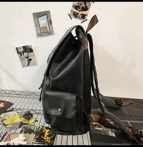 Detail view of black pebble leather backpack side pocket and brown nylon shoulder strap