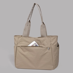 Detail of khaki tote bag showing a large zippered front pocket holding a smartphone
