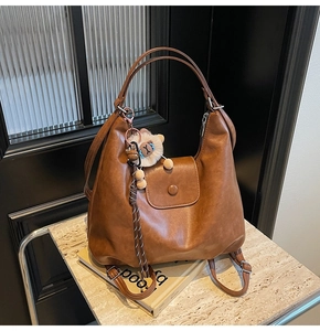 Close-up of brown faux leather tote bag with lion plush pendant on marble surface