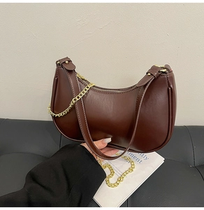 Detail of dark brown crescent underarm bag with smooth texture and gold chain strap