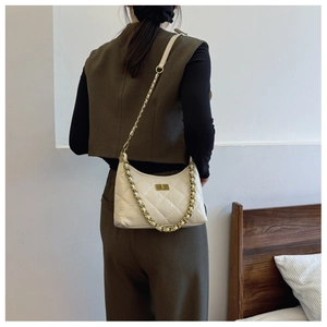 Detail of cream quilted dumpling bag with gold chain and turn-lock on a model