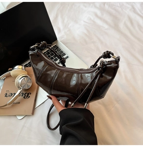 Macro detail of glossy coffee brown patent leather crescent bag with knot strap detail
