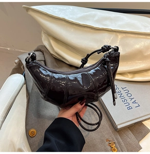 Detailed close-up of dark brown glossy patent leather croissant bag with silver zipper