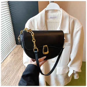 Detail view of black saddle bag featuring gold horseshoe buckle and chunky metal chain