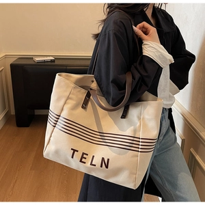 Detailed close-up of large canvas tote bag with brown leather straps and TELN logo