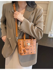 Brown monogram bucket bag with top handles and a dog charm accessory shown on a model
