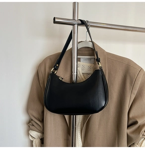 Detail of a black crescent shoulder bag with gold hardware styled on a beige blazer