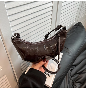 Detail of dark brown croissant bag showing glossy patent leather and knotted handle detail