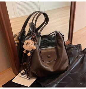 Detail of vintage brown leather tote bag featuring zipper closure and plush animal pendant