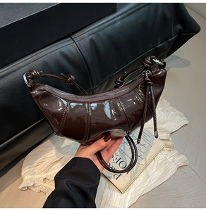 Close-up of a dark brown patent leather croissant bag featuring knotted shoulder strap