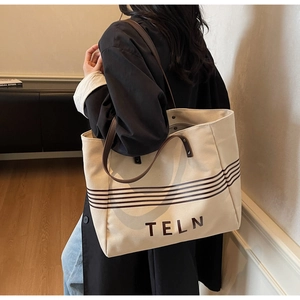 Detailed view of canvas tote bag with TELN logo and contrasting brown shoulder straps
