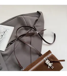 Detail of suede shoulder bag featuring a silver robot pendant on a grey blazer background