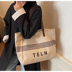 Detail of beige canvas tote bag with brown stripes and leather shoulder strap on model