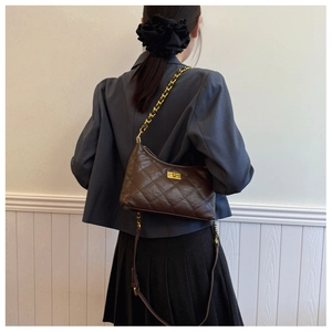 Detail of dark brown quilted leather shoulder bag with golden turn-lock on grey blazer
