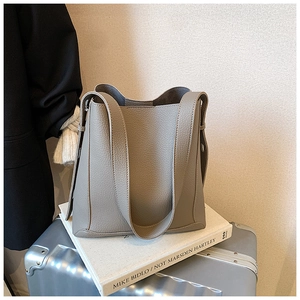 Detail of grey lychee leather bucket bag with top handle placed on a stylish silver suitcase