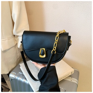 Detail of black leather saddle bag with trapezoid gold buckle and elegant chain strap