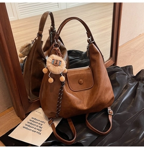 Detail of a brown vintage leather tote bag with a cute lion plush keychain and flap closure