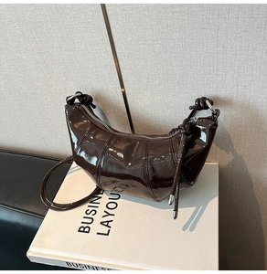 Detail of dark brown patent leather croissant bag with silver zipper and knot strap