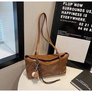 Detail of a brown glossy leather shoulder bag with a sporty baseball charm on white table