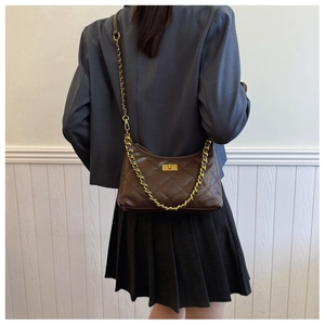 Close-up of quilted dark brown bag with gold chain strap worn over a grey suit