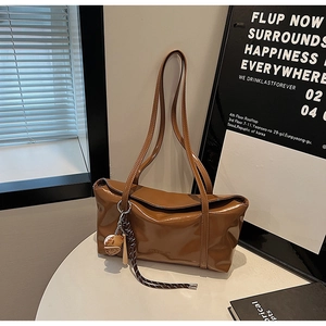 Detailed view of brown glossy shoulder bag with sleek strap and creative baseball charm
