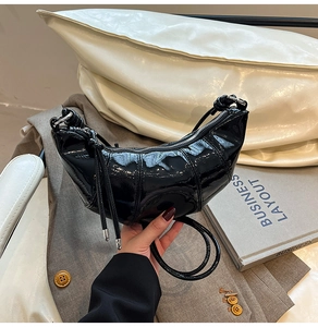 Detail shot of black patent leather crescent bag with segment stitching and silver zipper