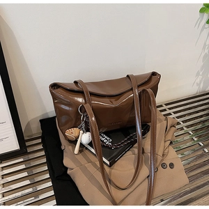 Detail of brown patent leather tote bag with sports charms on casual business attire