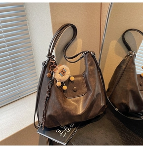 Close-up of brown leather hobo bag featuring a lion fur ball charm and woven cord detail