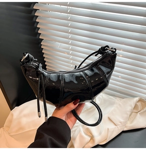 Detail of black glossy crescent bag with pleated stitching and stylish knot handle