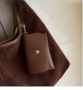 Detail of a dark brown leather detachable coin purse with a metal hook on a suede tote bag