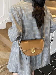 Brown leather saddle shoulder bag with gold clasp shown on a model in a casual suit