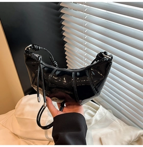Detail of glossy black patent leather crescent bag with pleated quilting and knot handle