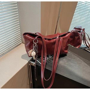 Detail of burgundy glossy PU leather tote bag with baseball charm in minimalist setting