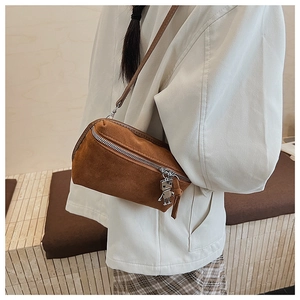Detail view of brown suede crossbody bag featuring a unique silver robot metal charm