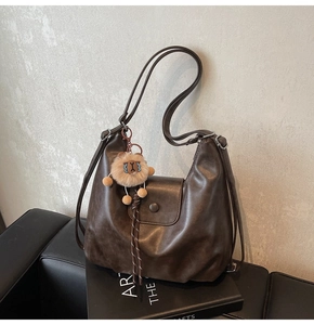 Detail view of deep brown vintage tote bag featuring a lion plush charm and magnetic flap