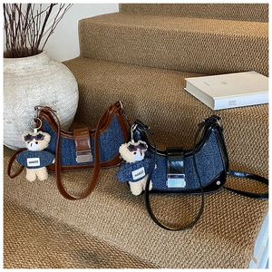 Detail of denim crossbody bag with leather trim and cute teddy bear charm accessory