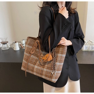 Grand sac cabas à carreaux marron avec bordure en cuir porté par un mannequin au café
