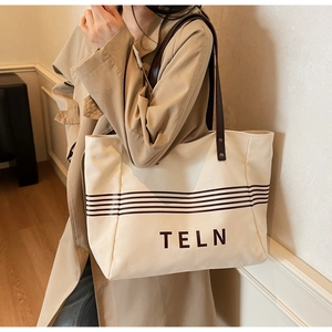 Chic cream canvas tote bag with brown stripes and leather straps shown on a model