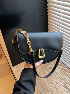Chic black saddle bag with gold metal buckle and leather chain strap shown in hand