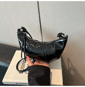 Detailed close-up of shiny black patent leather croissant bag with silver zipper detail