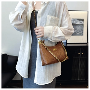 Brown quilted dumpling bag worn by model featuring gold chain strap and turn-lock