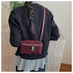 Detail view of burgundy faux suede crossbody bag featuring a silver robot pendant charm