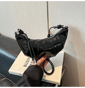 Detail of glossy black patent leather croissant bag with knotted handle and zip closure