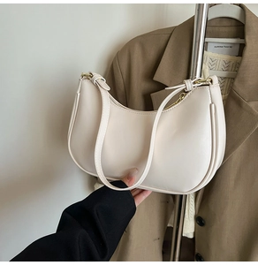 Detail of a creamy white half-moon underarm bag with gold hardware and smooth leather finish