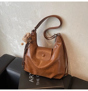 Detail view of brown vintage Hobo bag with plush pom-pom charm and adjustable strap