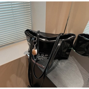 Close-up of black patent leather shoulder bag with a creative baseball glove charm