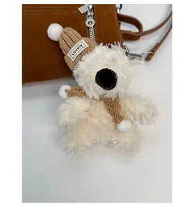 Detail eines cremeweißen Plüschbär-Anhängers mit brauner Strickmütze und Schal für Taschen