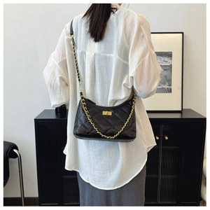 Detail shot of black quilted faux leather crossbody bag with gold chain strap on model