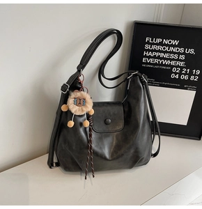 Detail of black matte PU leather hobo bag featuring a cute lion plush pendant decoration