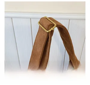 Detail of adjustable suede shoulder strap with vintage brass buckle on brown tote bag